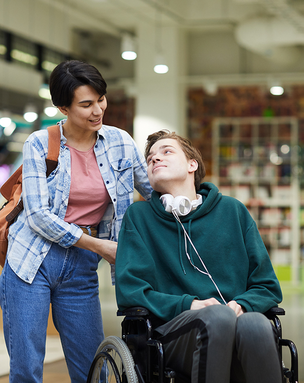 Young man with disability looking at carer who is pushing his wheelchair