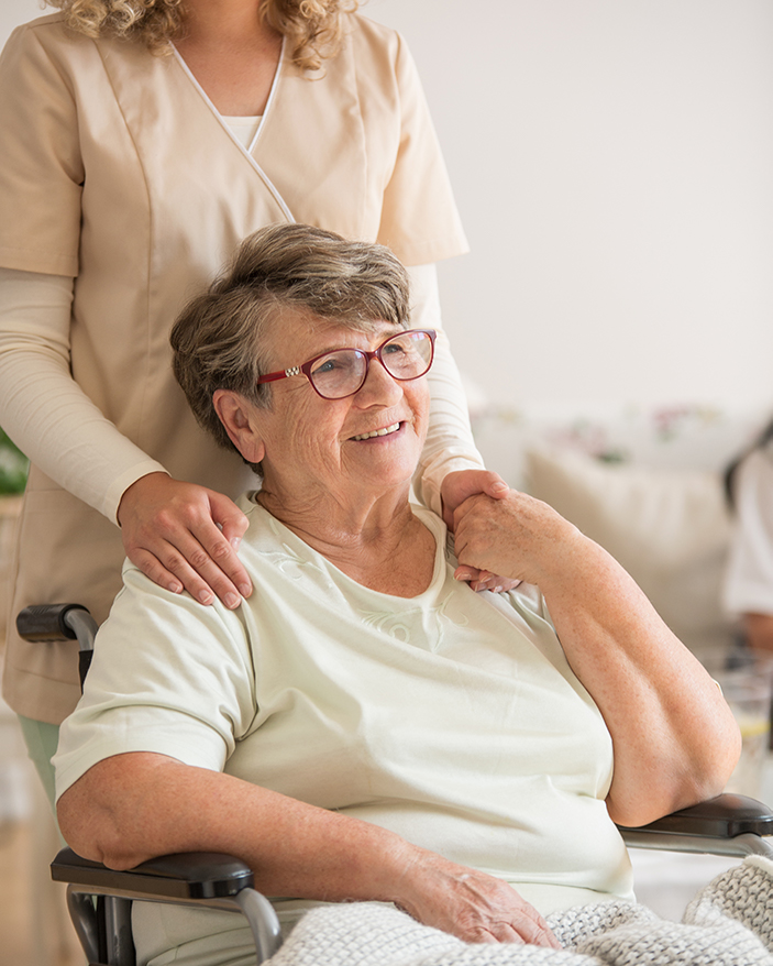 Woman standing behind senior woman in wheelchair with hands on her shoulders