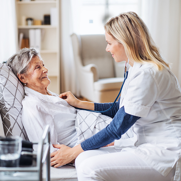 A healthcare professional smiling and interacting with an elderly patient in a cozy living room, showcasing compassionate care and professional support.