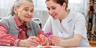 A caregiver smiling while handing a tray to an elderly woman in a warmly lit living room, highlighting the importance of compassionate elderly care.