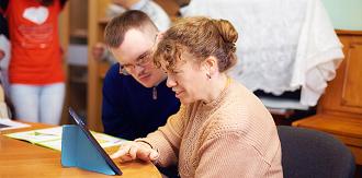 An elderly woman and a caregiver engaging in a playful activity, assembling colorful puzzle pieces together at a table.