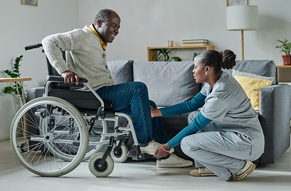 Woman helping man lift feet into wheelchair footplate